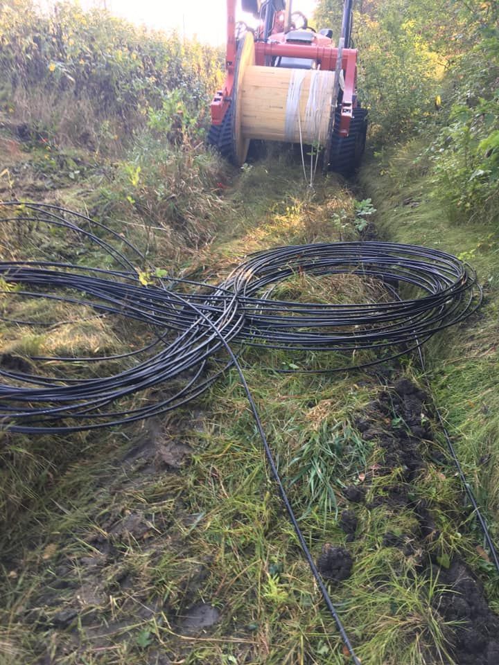 Tractor pulling a cable spool in a grassy ditch; black cables are coiled on the ground.