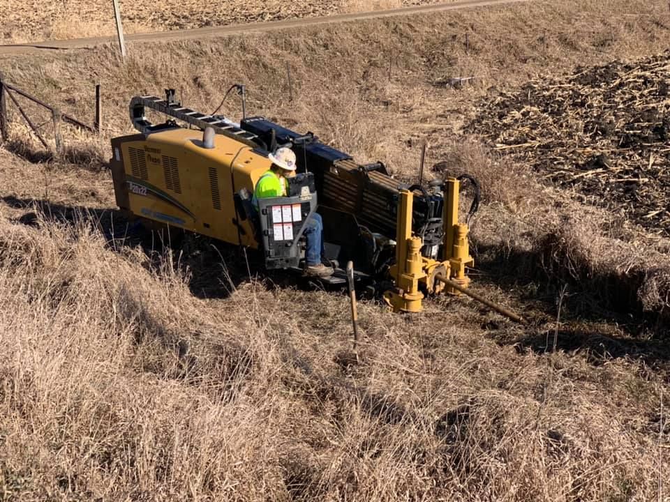Yellow drilling machine on a hillside, operator in the seat. Dry grass surrounds it.