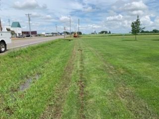 Green grassy field with a road and buildings in the background on a cloudy day.