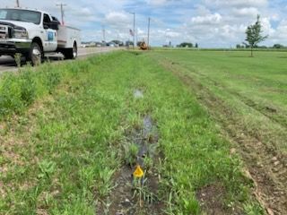 A utility truck parked beside a grassy ditch with standing water; rural setting under a partly cloudy sky.
