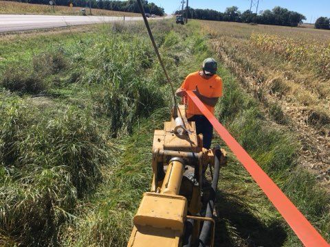 Man operating machinery laying orange cable beside a road and field.