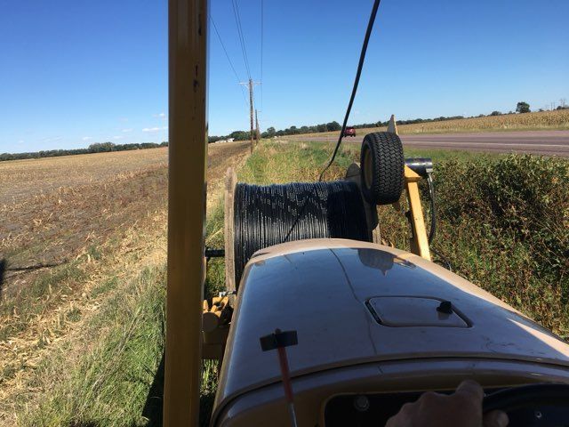 A tractor pulling a spool of black cable beside a road with power lines overhead.