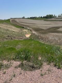 Grassy landscape with a dry ditch and fields in the background under a blue sky.