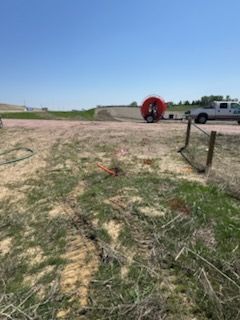 Red cable reel, truck, and construction equipment on dirt road and grassy field under a blue sky.