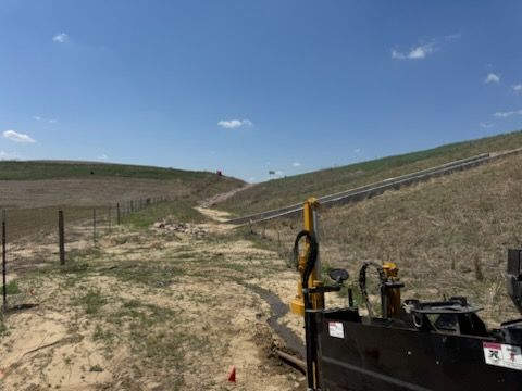Construction site with a pipeline. A machine in the foreground, sloped land, blue sky.