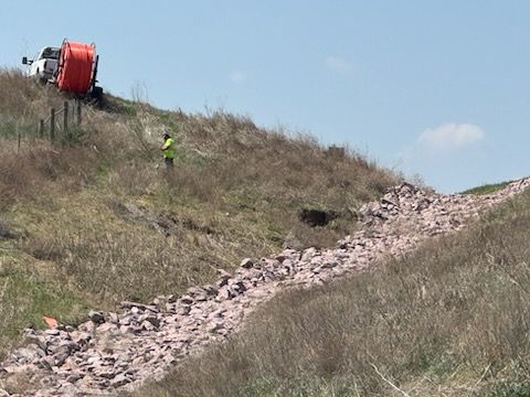 A truck with an orange container on a hillside with a stone-lined channel, and a worker in a safety vest.