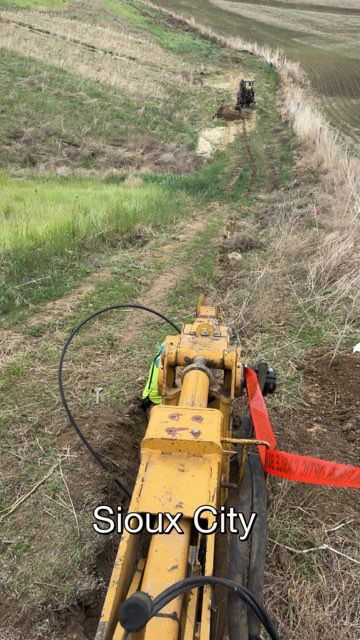 Trenching machine excavating a trench in a field near Sioux City, Iowa, with other machinery in the background.