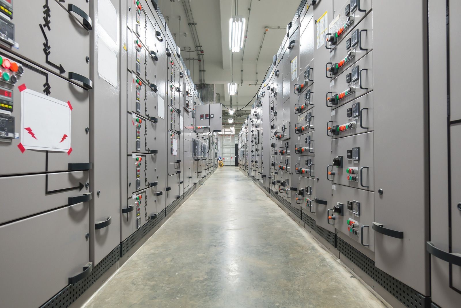 Rows of electrical control panels in a long, brightly lit corridor.