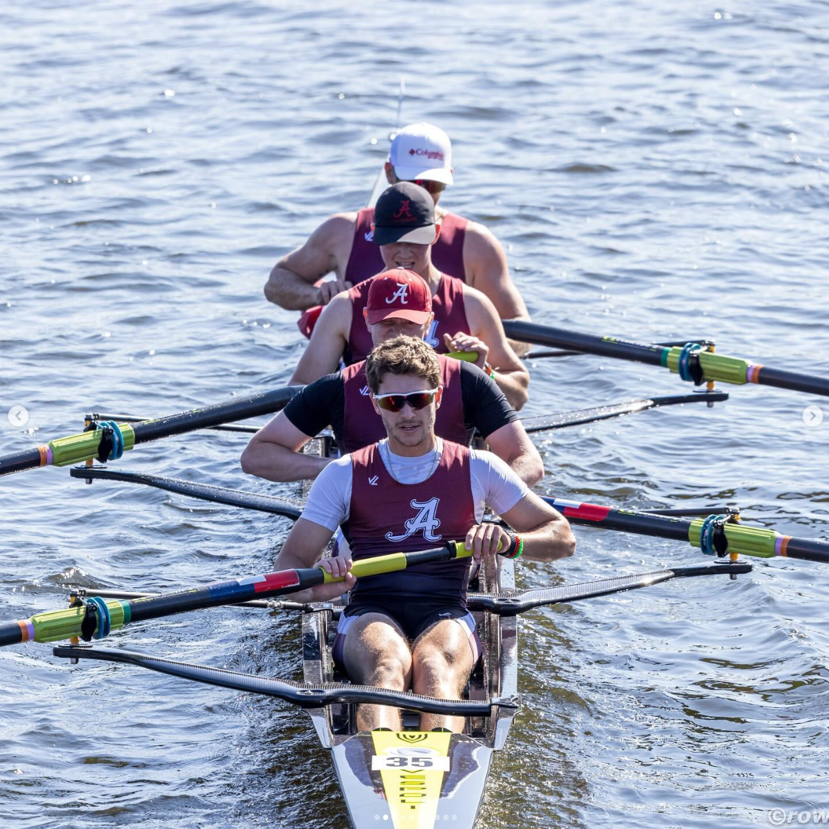 Rowing team on water, wearing maroon and white.  Four men in a boat, rowing in unison.