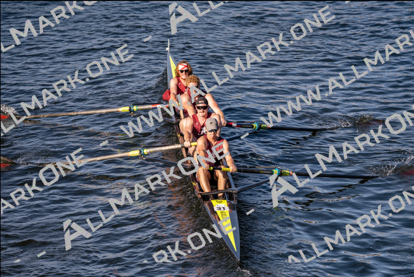 A rowing crew of four in a sleek boat on water, pulling oars. They wear red and white uniforms.