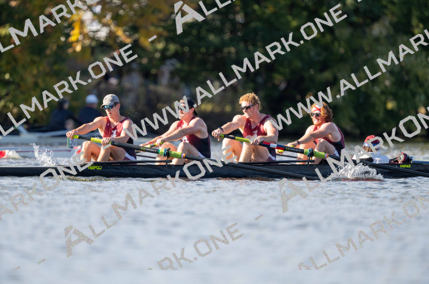 A rowing team of four women in maroon and navy uniforms on a dark boat, powering through water. They are in a race.