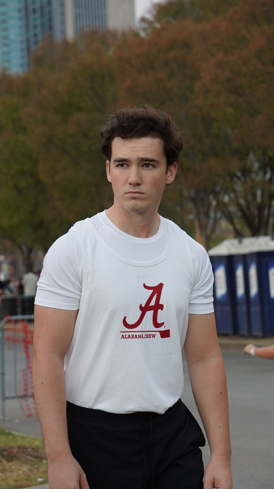 A young man wearing a white t-shirt with an Alabama logo stands outside, looking to the side.
