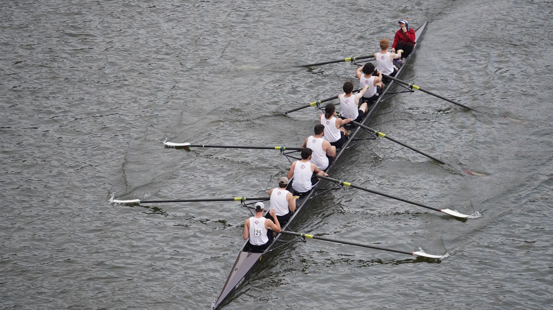 A rowing team of eight people in a long boat on a river. They are all rowing in unison.