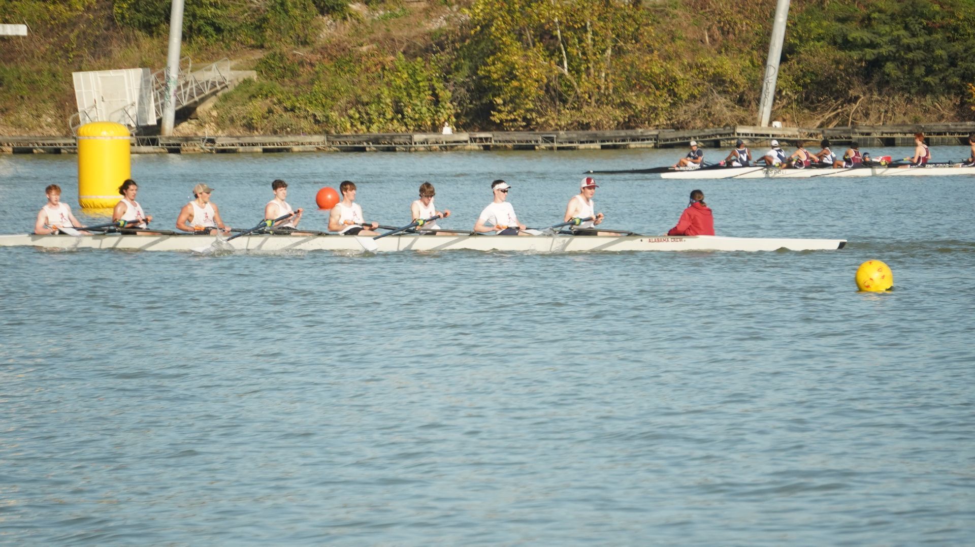 A rowing team of eight people in a long white boat on a river, competing in a race on a sunny day.