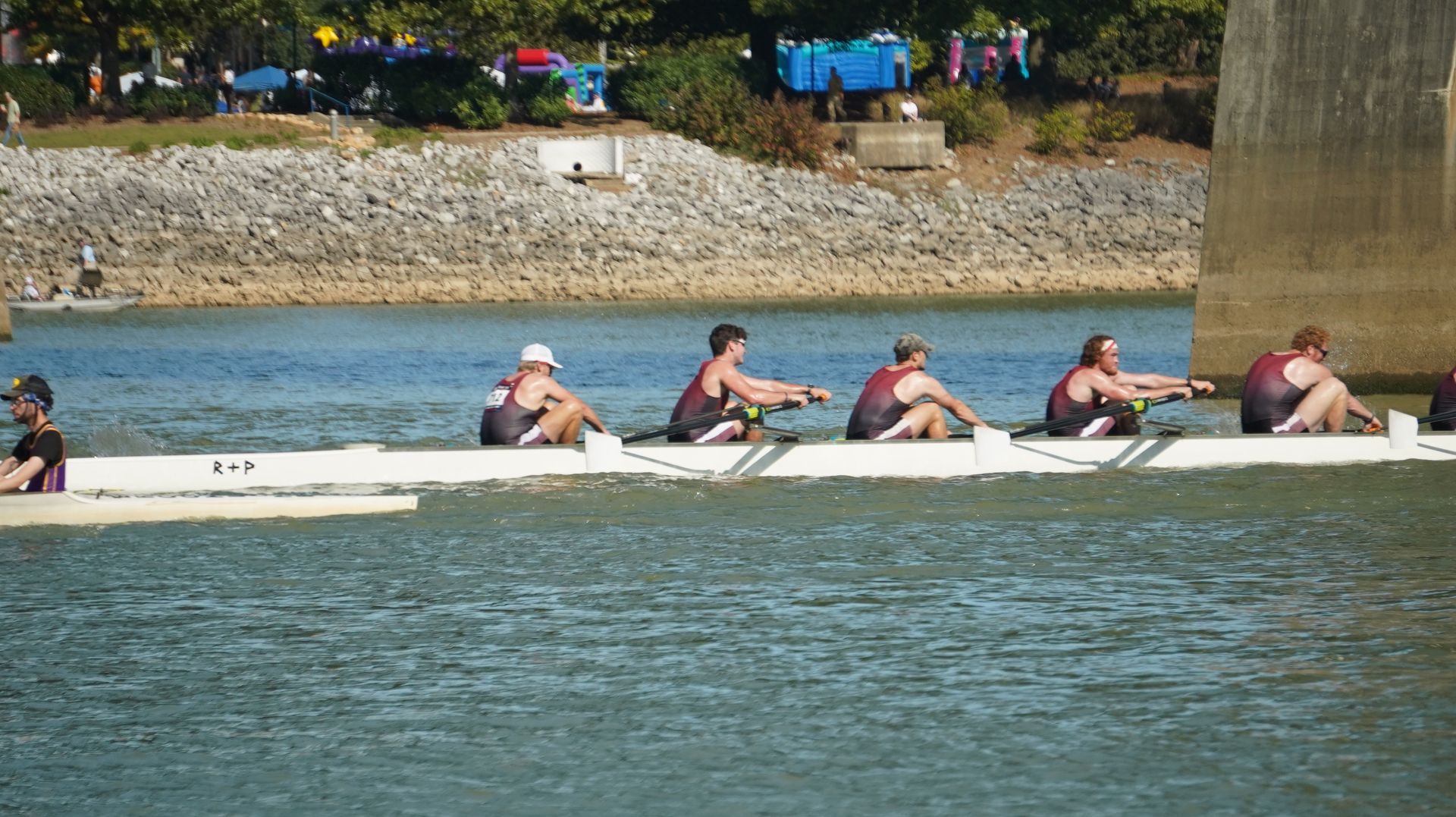 A rowing team in a white boat glides across a river. They row in unison.