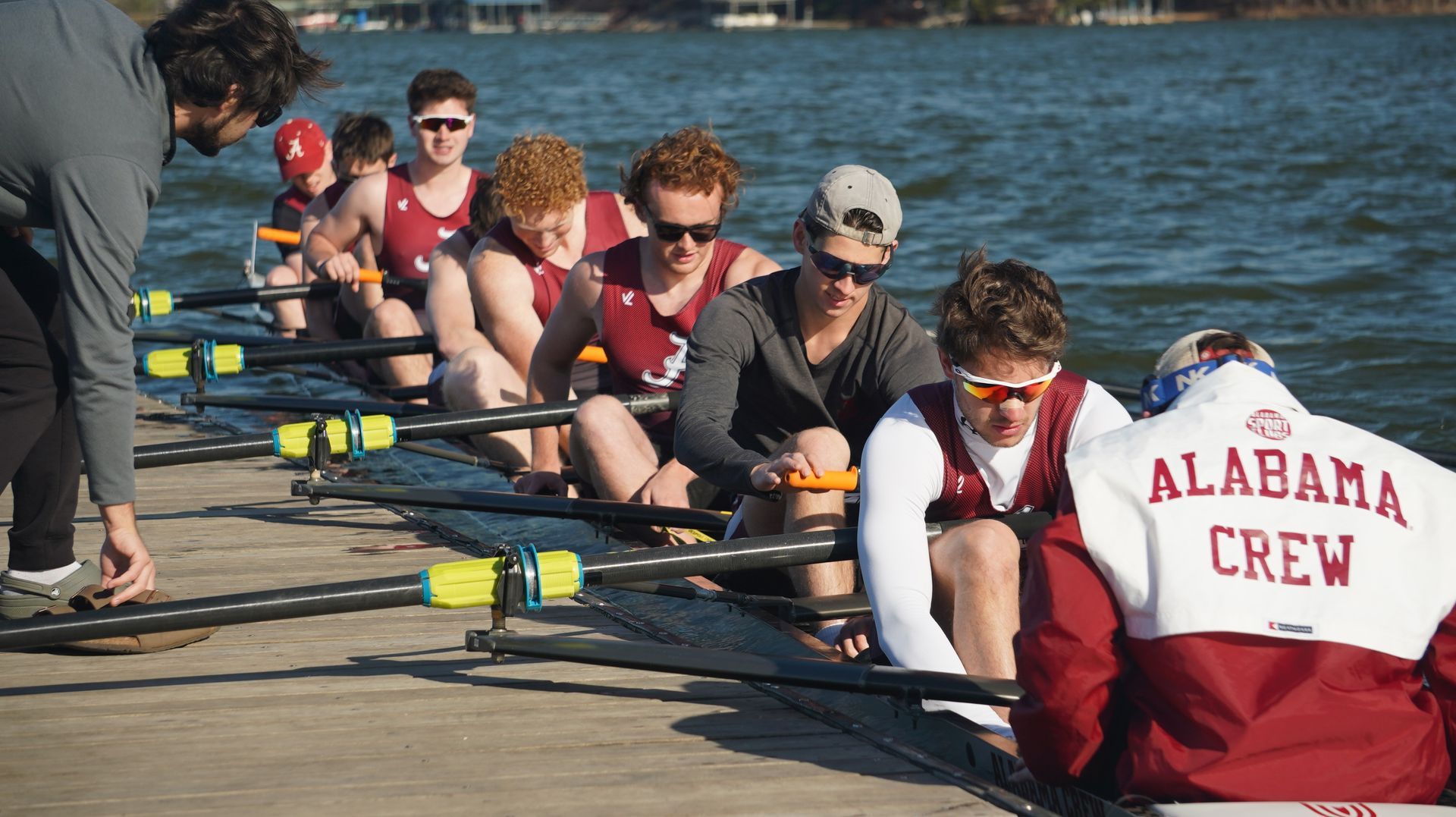 A rowing team in maroon and white uniforms, coached on a dock. 