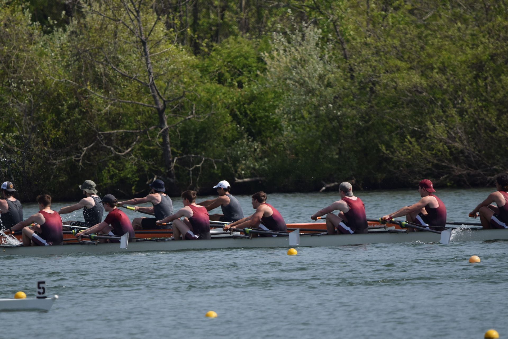 Two rowing teams in boats on a river, competing. The teams wear matching outfits with dark tops and bottoms. 