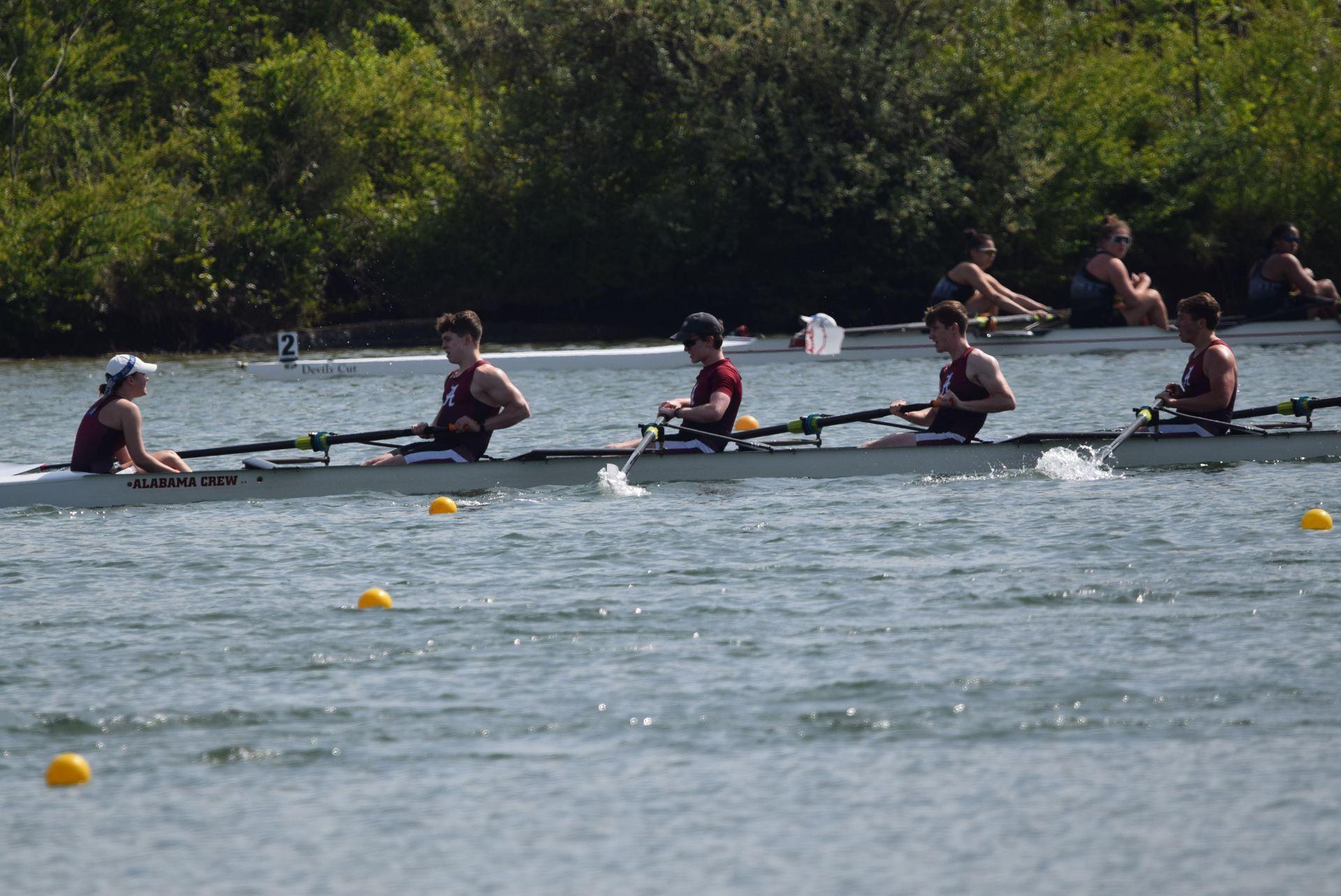 Rowing crew racing on a river. Four rowers in a boat, splashing water, with spectators on the bank.
