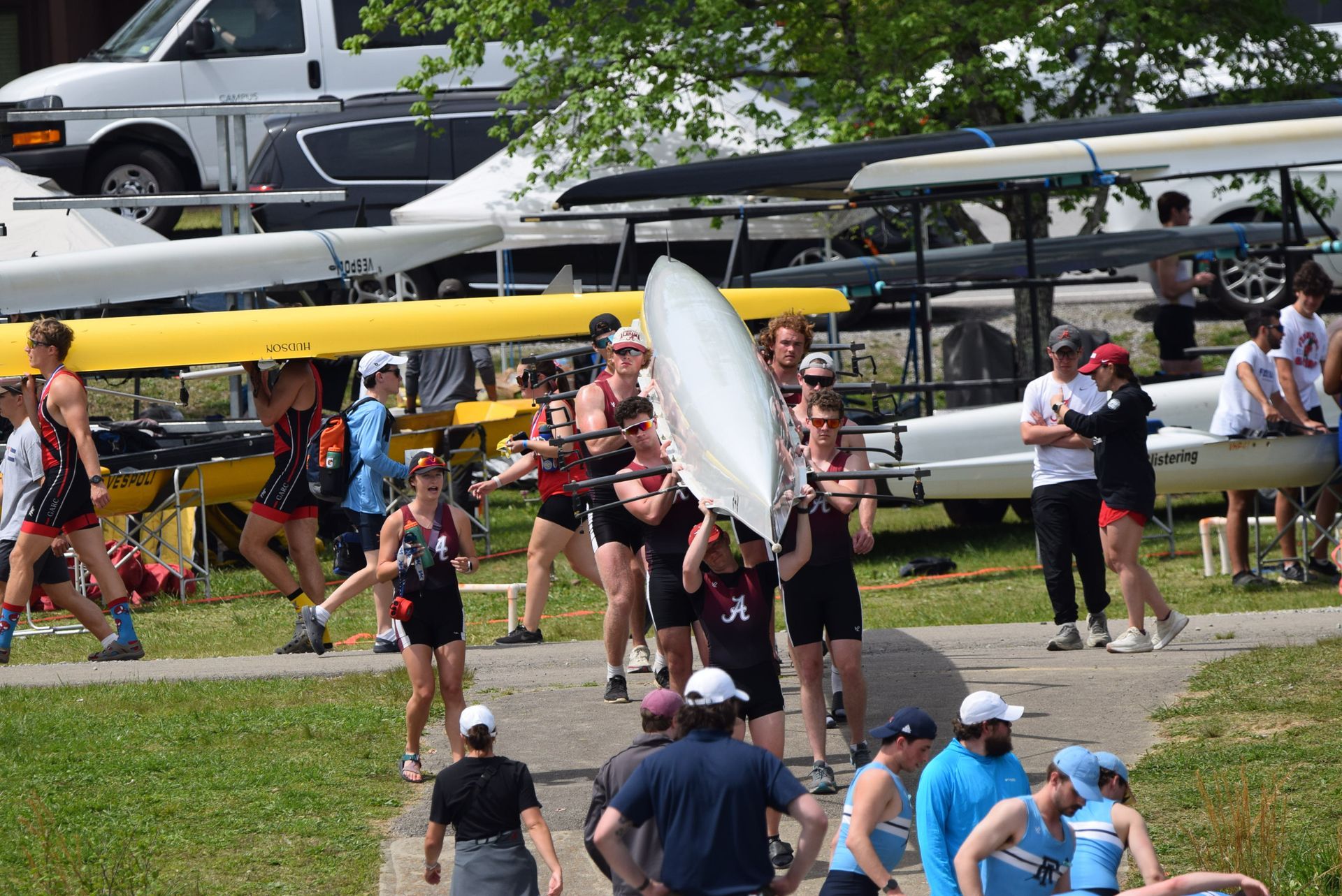 Rowing team carrying a boat overhead. Athletes in athletic wear are outdoors near a dock.
