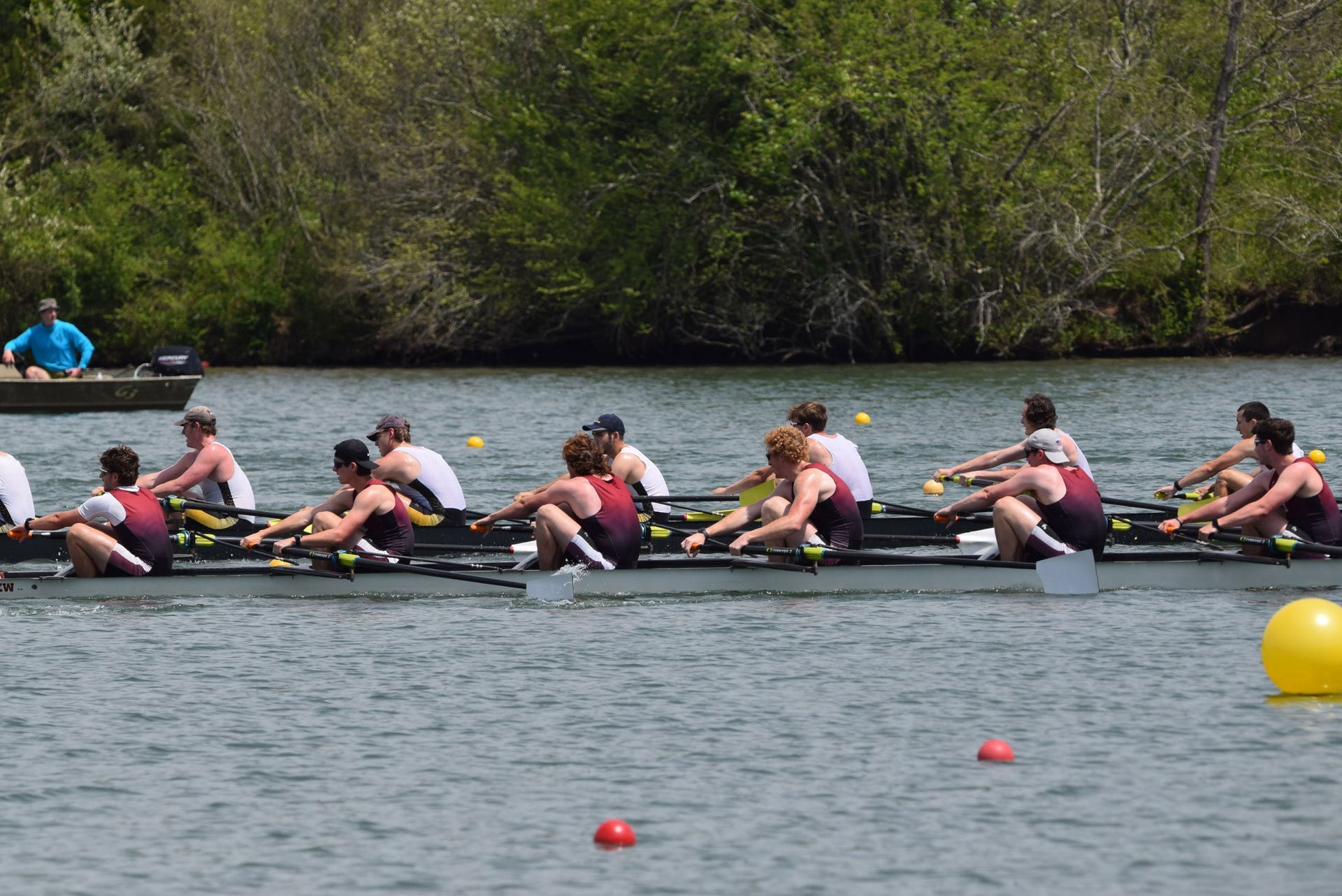  Rowers in maroon and white uniforms propel their boat towards the finish line near a yellow buoy.