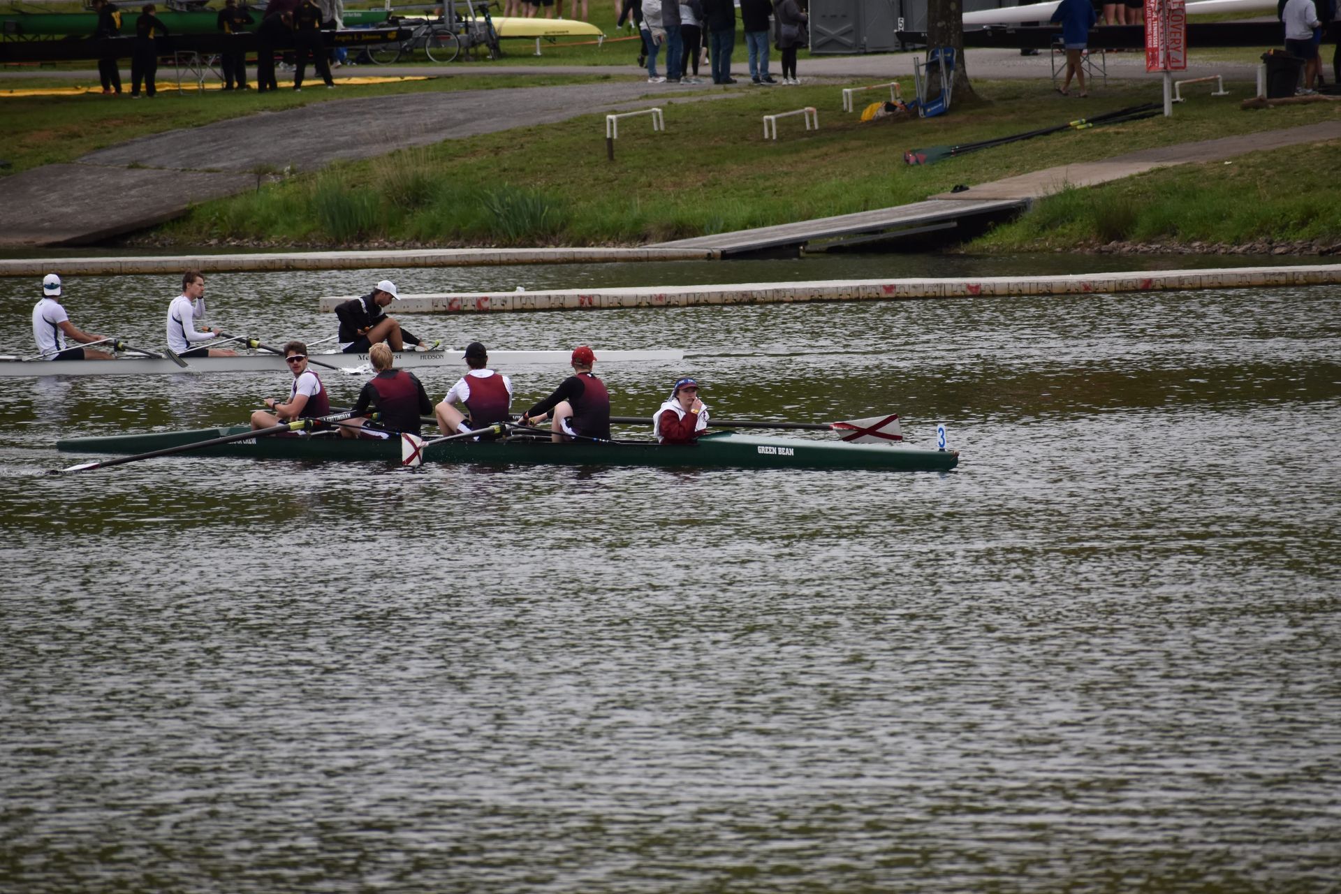 A rowing crew competes on a lake.  The crew is in a long, green boat, and the rowers are wearing matching team uniforms.