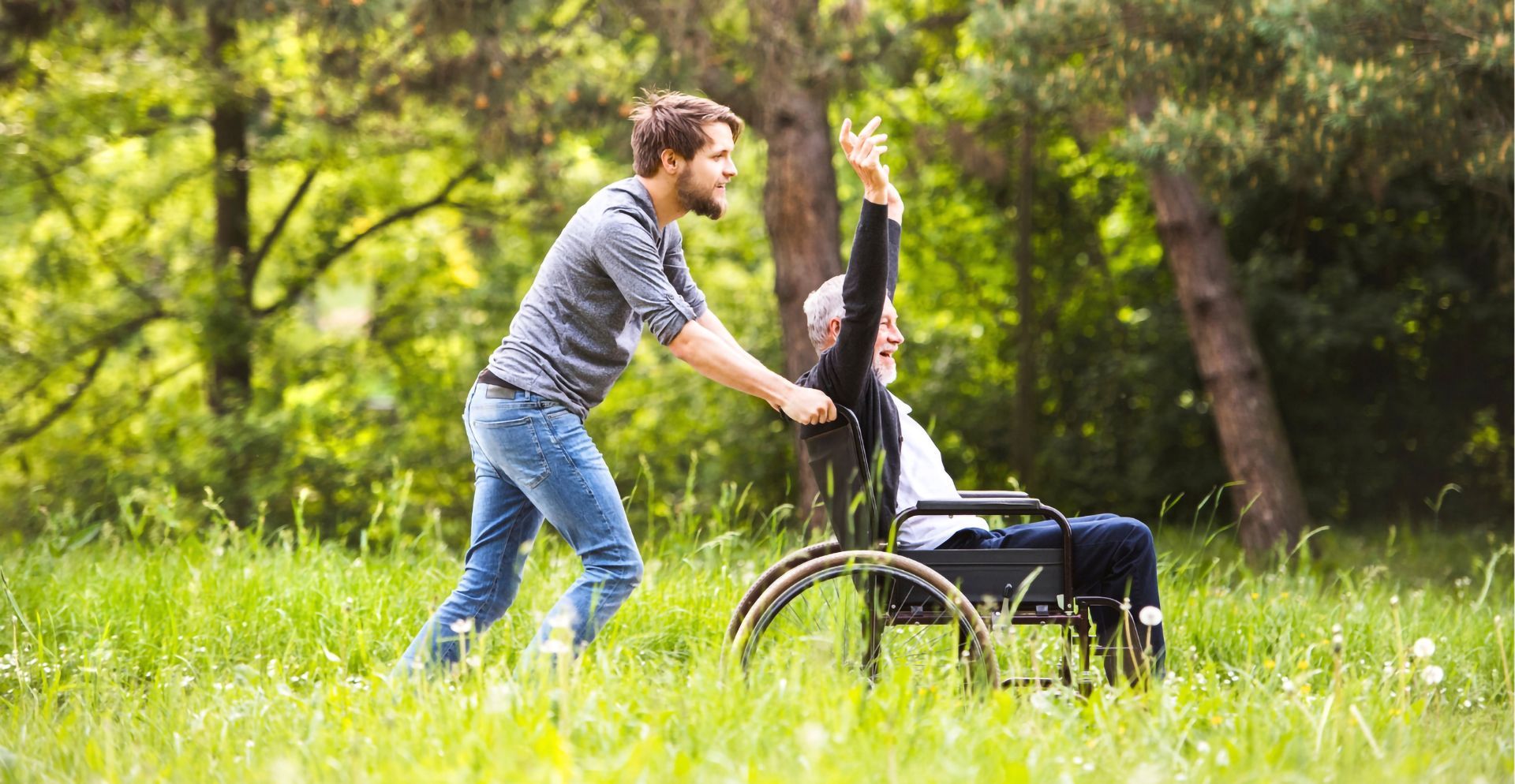 Young man pushing an older man in a wheelchair through grass