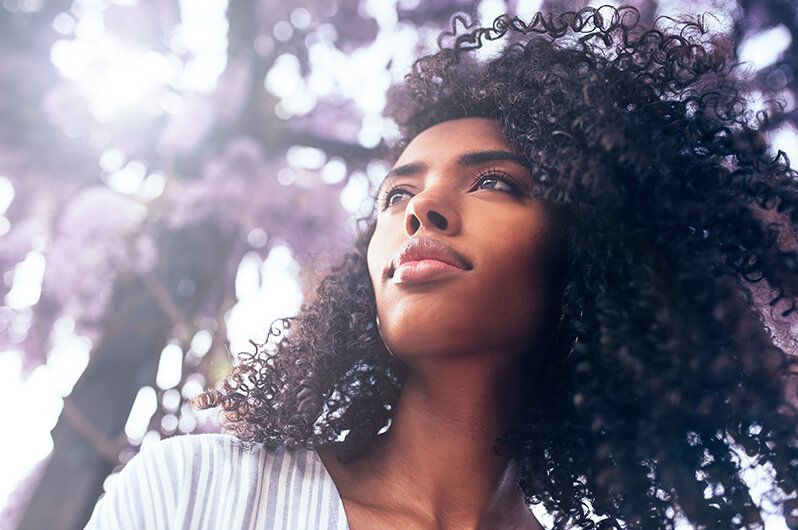 A woman with curly hair is looking up at a tree with purple flowers.