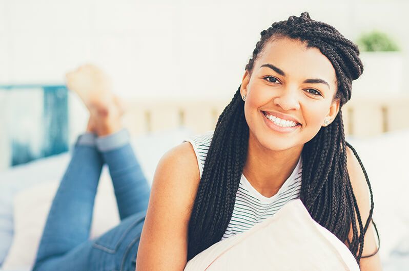 A woman is laying on her stomach on a bed holding a pillow and smiling.