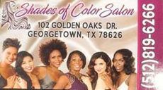 A group of women are posing for a picture in front of a sign for shades of color salon.