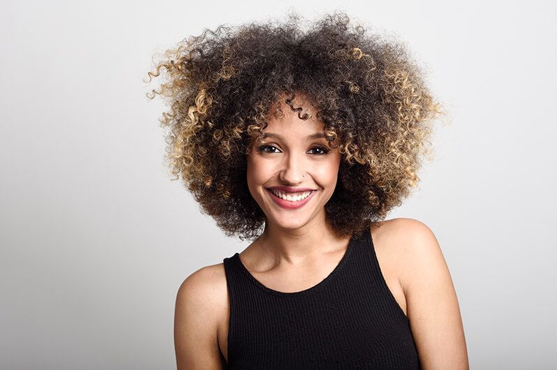 A woman with curly hair is smiling and wearing a black tank top.