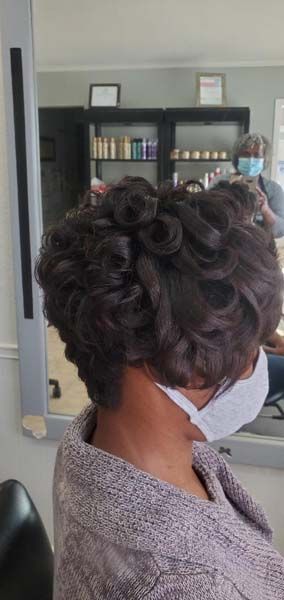 A woman wearing a face mask is getting her hair done in a salon.