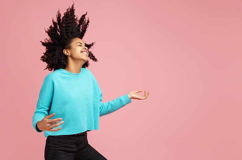 A woman in a blue sweater is dancing with her hair in the air.