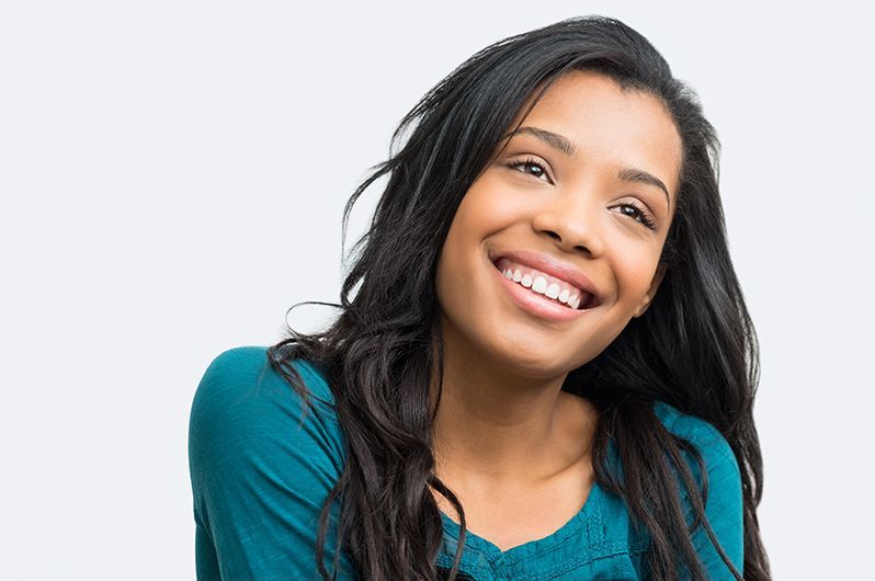 A woman in a blue shirt is smiling and looking at the camera.