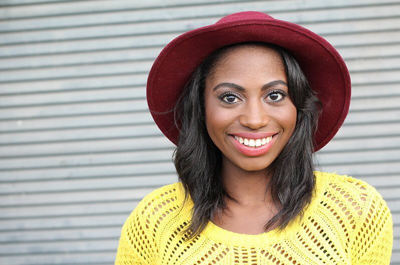 A woman wearing a yellow sweater and a red hat is smiling.