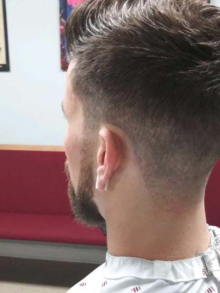 A man with a beard is getting his hair cut at a barber shop.
