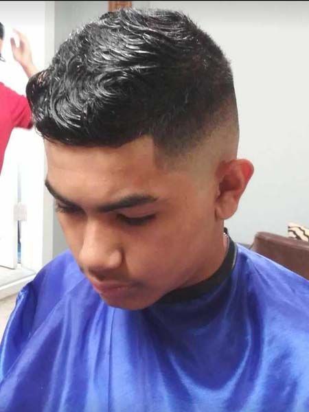 A young man is getting his hair cut at a barber shop.