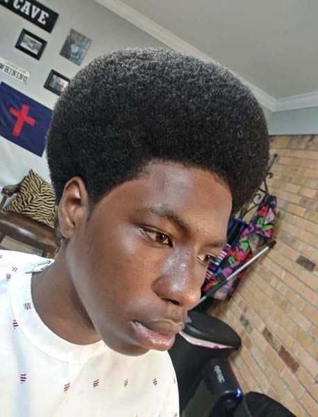 A young man with a large afro is standing in front of a sign that says cave