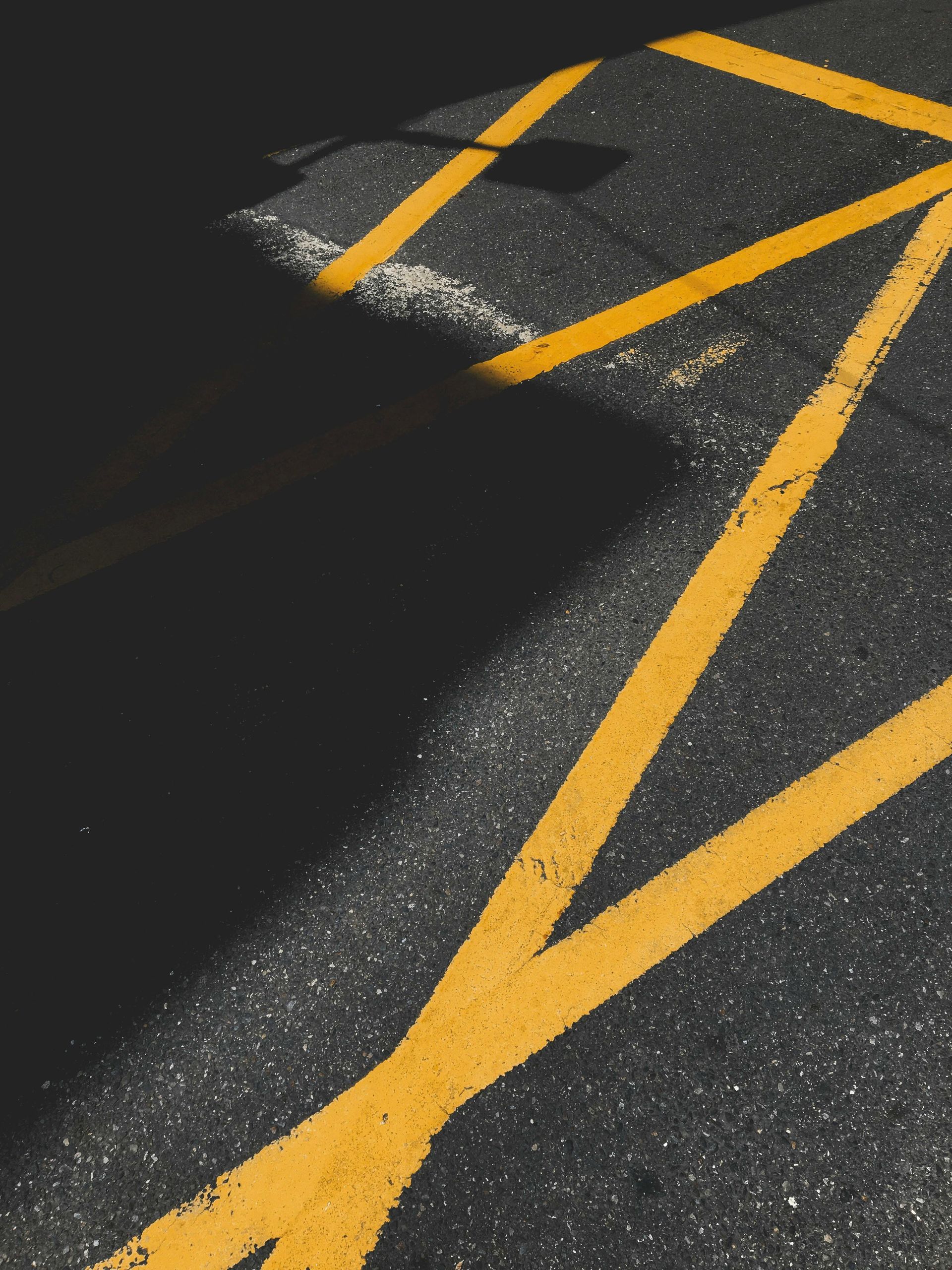 Yellow no-parking lines on dark asphalt. A large shadow is cast on the left.