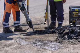 Two workers repairing asphalt with a jackhammer, standing near a generator.