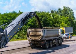 Road milling machine loading asphalt into a dump truck on a sunny day.