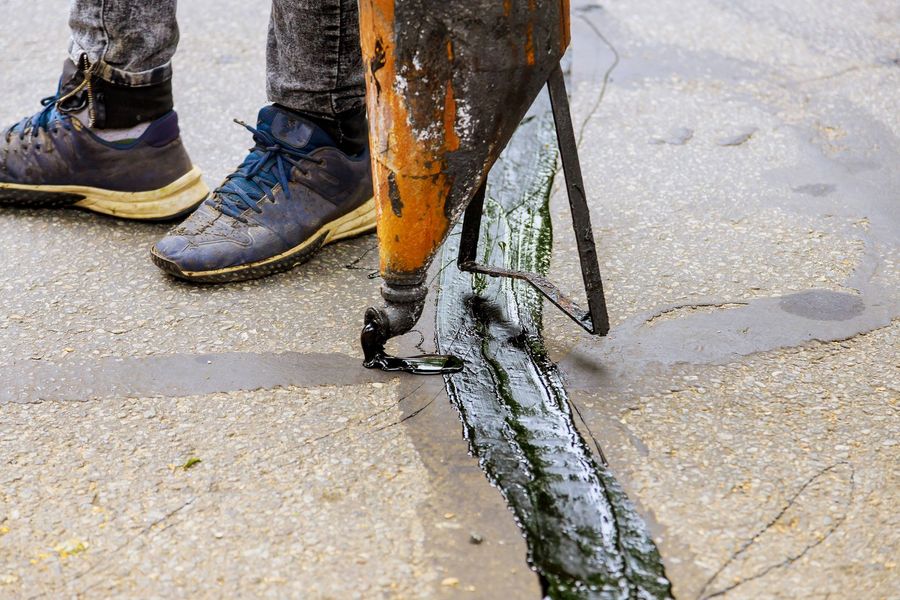 Person pouring sealant into crack in pavement with orange applicator.