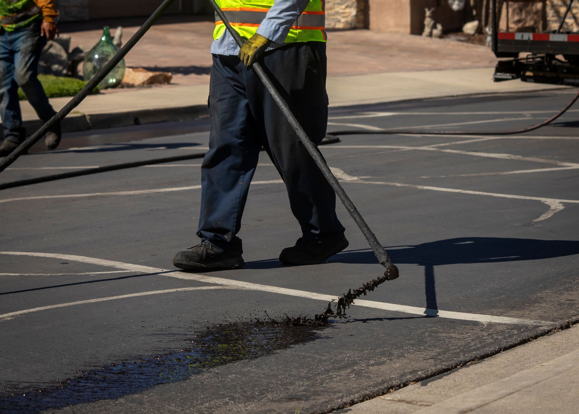 Construction worker in safety vest using a rake to spread asphalt on road surface, near a white line.
