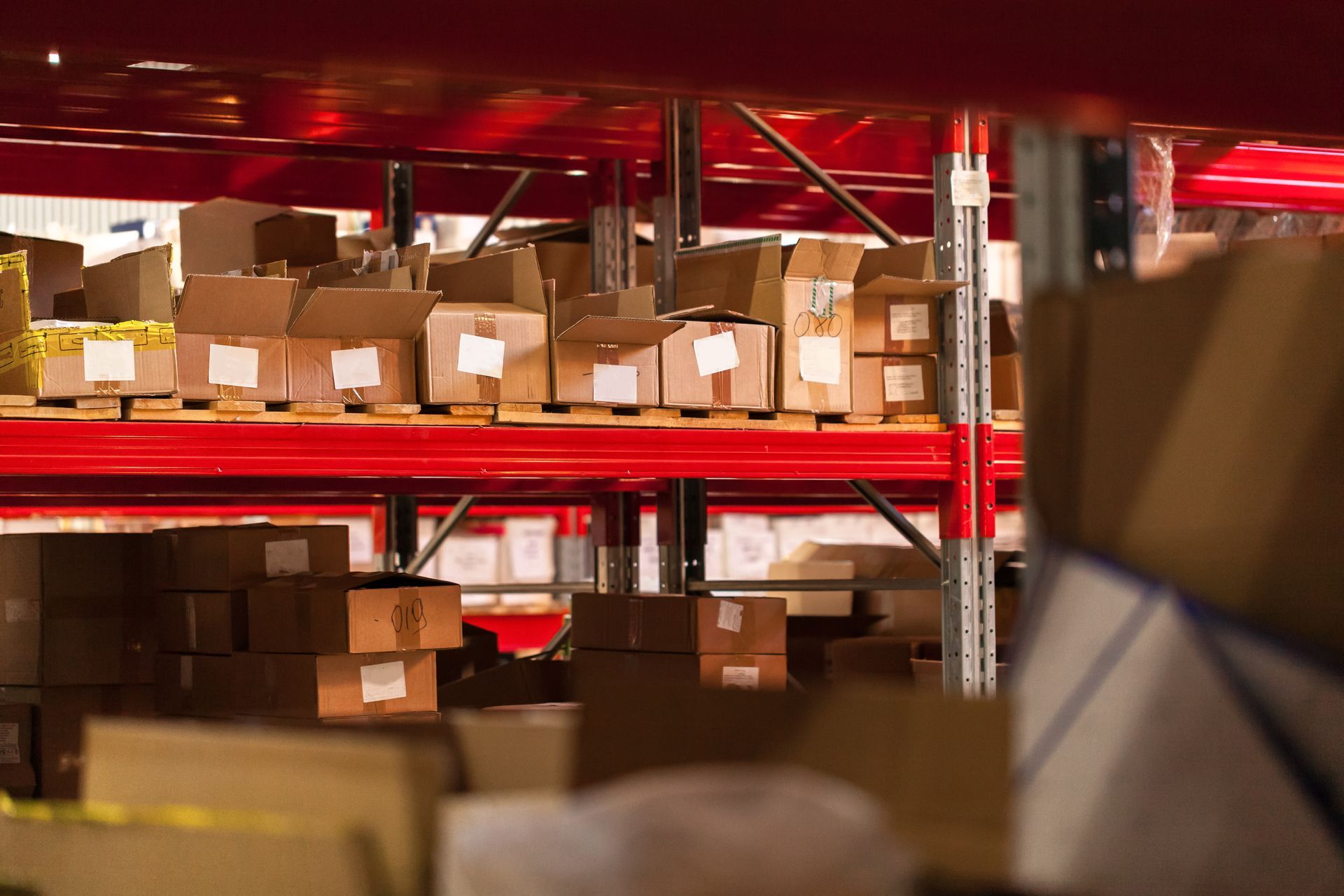 A warehouse filled with lots of cardboard boxes on red shelves.