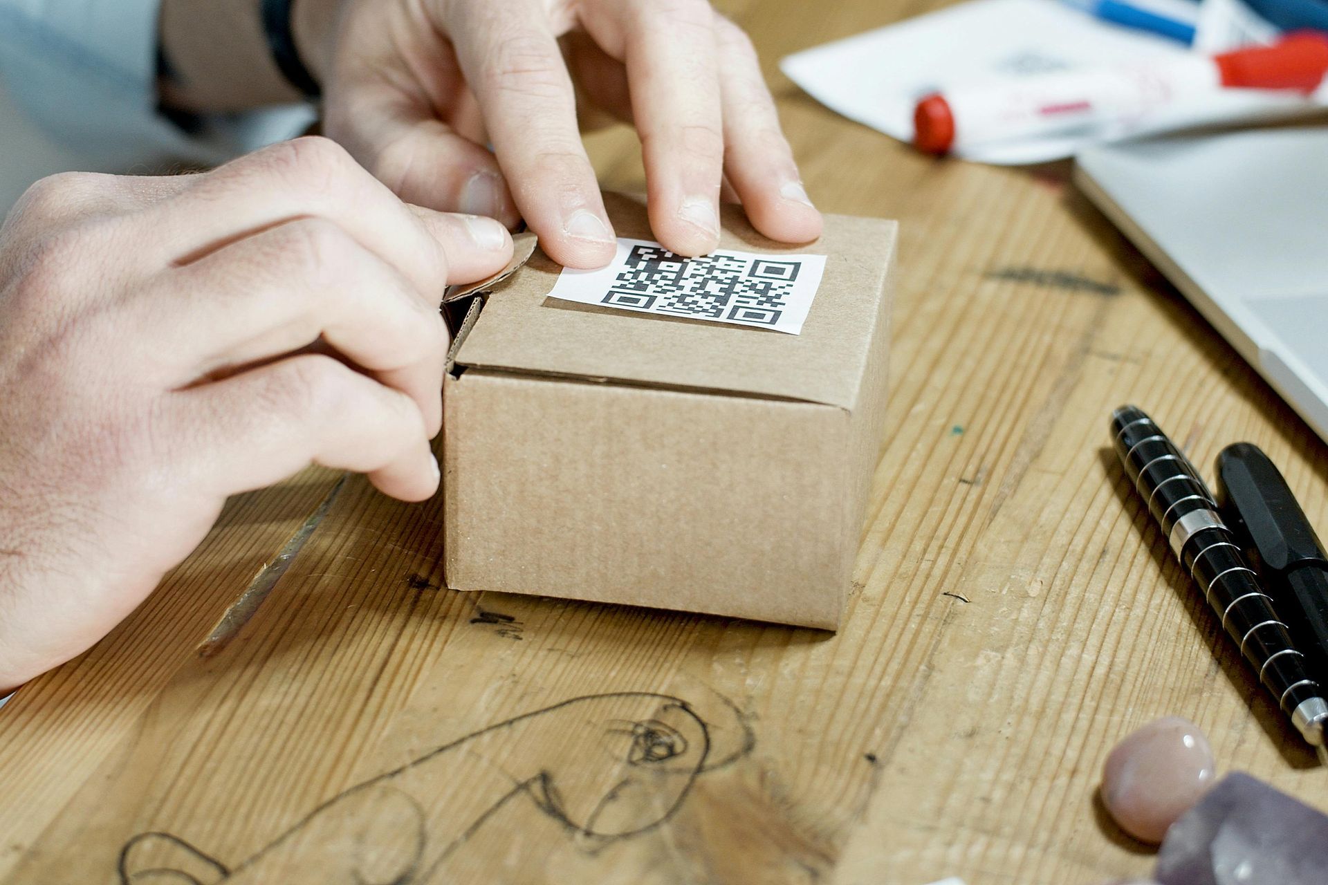 Hands placing shipping label with QR code on brown package box during fulfillment process