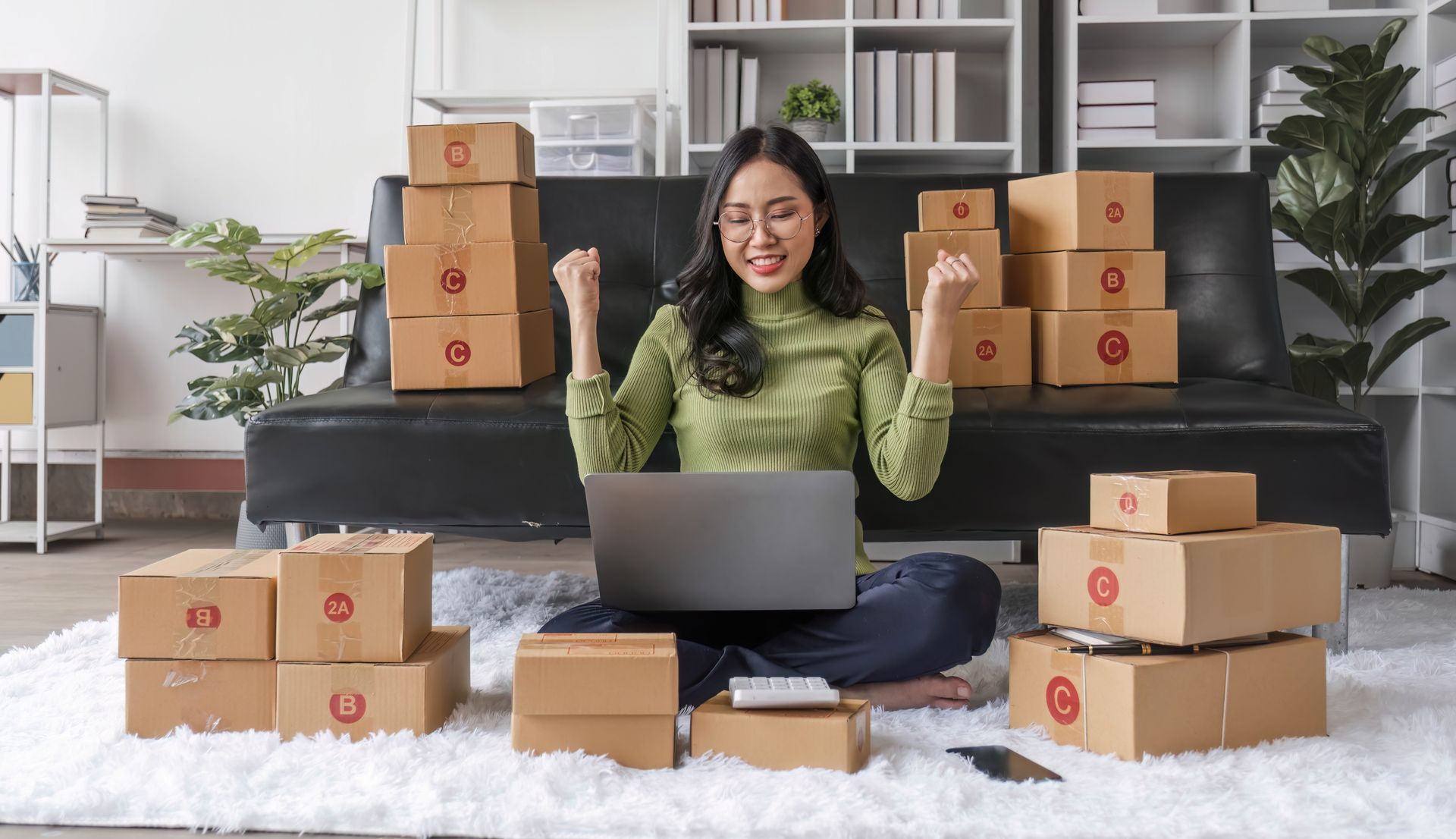 A woman is sitting on the floor using a laptop computer surrounded by boxes.