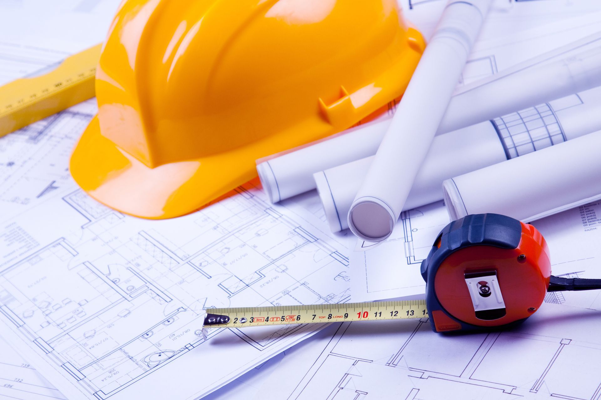 A yellow hard hat is sitting on top of blueprints next to a tape measure.