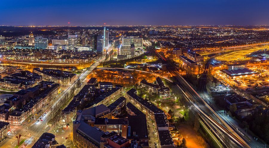 Een nachtelijke luchtfoto van een stadsgezicht met verlichte gebouwen, gloeiende straatlantaarns en druk verkeer op de snelweg.