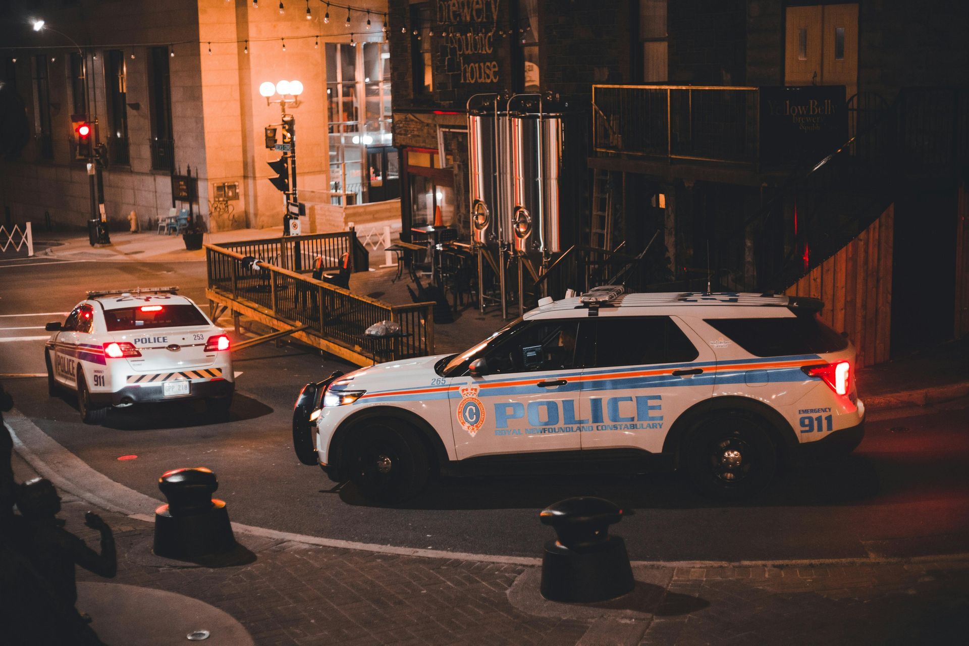 Two police cars on a city street at night. One car is turning, the other is driving straight.