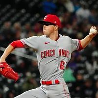 Cincinnati Reds pitcher throwing a baseball, wearing red and gray uniform, cap, and sunglasses.