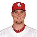 A smiling baseball player wearing a red Cardinals cap and jersey.